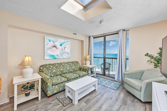 living room with a water view, light hardwood / wood-style floors, a textured ceiling, and a wall of windows