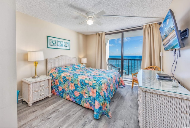 bedroom featuring access to exterior, ceiling fan, expansive windows, hardwood / wood-style floors, and a textured ceiling