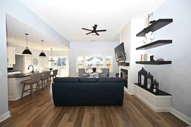 living room with dark hardwood / wood-style flooring, a fireplace, ceiling fan with notable chandelier, and sink