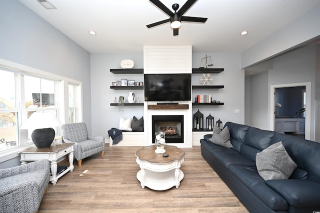 living area with light wood-style flooring, visible vents, a large fireplace, and ceiling fan