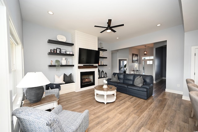 living room featuring ceiling fan, a large fireplace, and hardwood / wood-style flooring