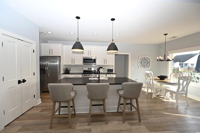 kitchen with white cabinets, decorative light fixtures, a center island with sink, and appliances with stainless steel finishes