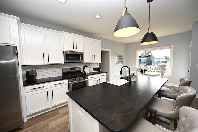 kitchen featuring dark countertops, a sink, dark wood-type flooring, decorative backsplash, and appliances with stainless steel finishes