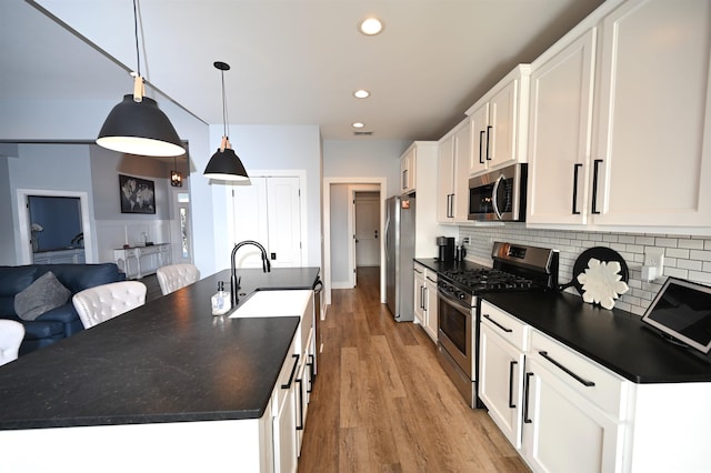kitchen featuring recessed lighting, stainless steel appliances, backsplash, dark countertops, and a center island with sink