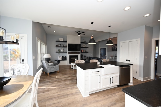 kitchen with stainless steel dishwasher, a ceiling fan, dark countertops, a sink, and light wood-type flooring