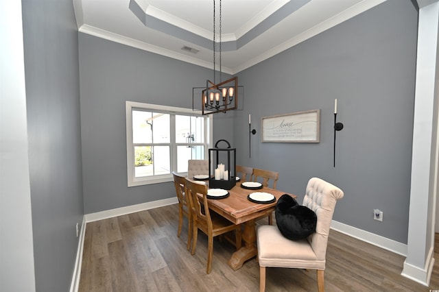 dining area featuring a tray ceiling, dark hardwood / wood-style flooring, a chandelier, and ornamental molding