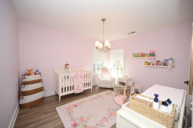 bedroom with wood finished floors, visible vents, a crib, and a notable chandelier