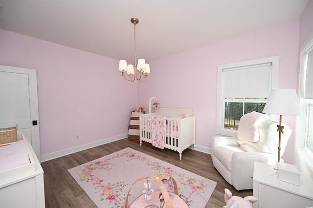 bedroom featuring a chandelier, a nursery area, baseboards, and dark wood-style floors