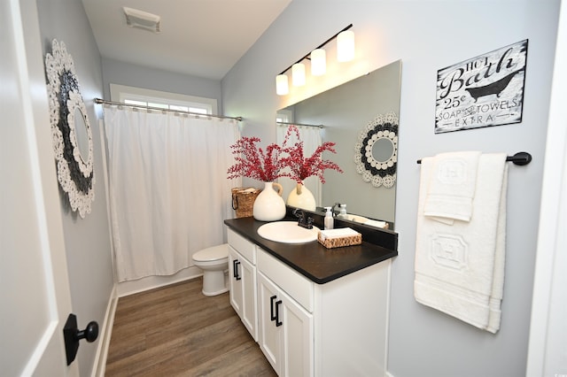 full bathroom with toilet, visible vents, baseboards, wood finished floors, and vanity