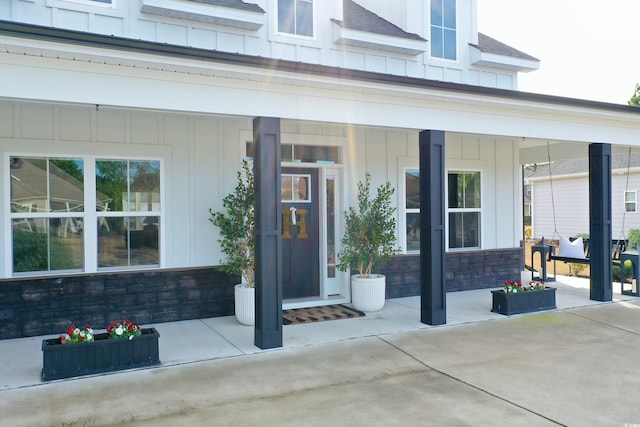 entrance to property featuring stone siding, a porch, roof with shingles, and board and batten siding