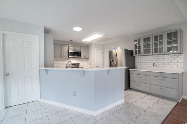 kitchen featuring kitchen peninsula, appliances with stainless steel finishes, light tile patterned floors, and gray cabinetry