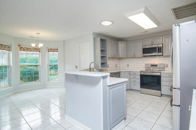 kitchen with appliances with stainless steel finishes, decorative light fixtures, an inviting chandelier, and gray cabinetry