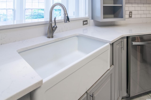 details with backsplash, light stone counters, dishwasher, and sink