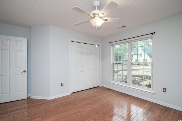 unfurnished bedroom with a closet, light hardwood / wood-style flooring, ceiling fan, and a textured ceiling