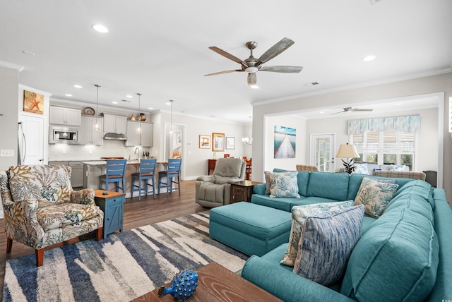 living area with ornamental molding, a ceiling fan, recessed lighting, and wood finished floors