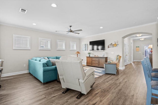 living area featuring arched walkways, a ceiling fan, wood finished floors, visible vents, and ornamental molding