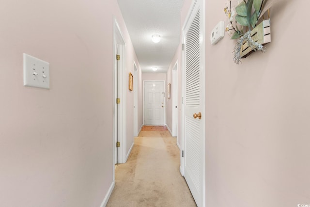 corridor with light colored carpet and a textured ceiling