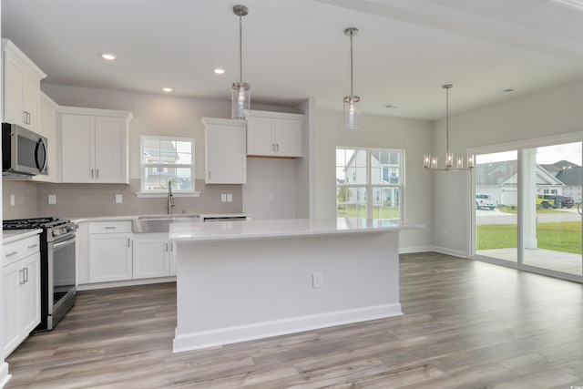 kitchen featuring a kitchen island, a notable chandelier, a healthy amount of sunlight, white cabinetry, and stainless steel appliances