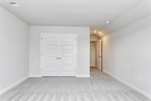 unfurnished bedroom featuring light colored carpet, vaulted ceiling, and a closet