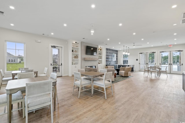 dining room with a fireplace, french doors, light wood-type flooring, and built in shelves