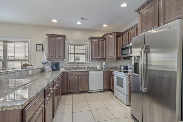 kitchen with sink, stainless steel appliances, stone countertops, dark brown cabinets, and light tile patterned floors