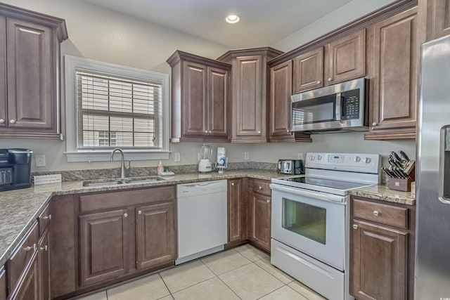 kitchen featuring appliances with stainless steel finishes, light stone counters, dark brown cabinets, sink, and light tile patterned flooring