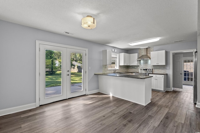 kitchen with electric stove, wall chimney range hood, white cabinetry, decorative backsplash, and kitchen peninsula