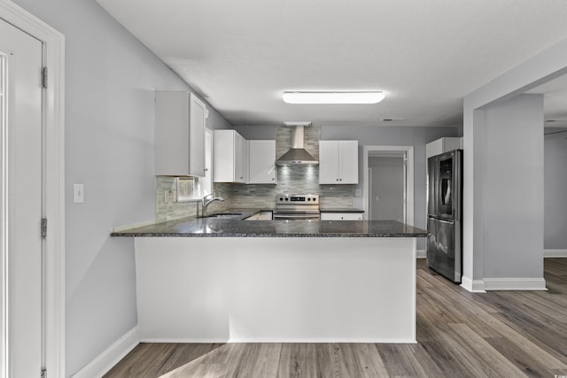 kitchen with sink, wall chimney range hood, kitchen peninsula, white cabinets, and appliances with stainless steel finishes