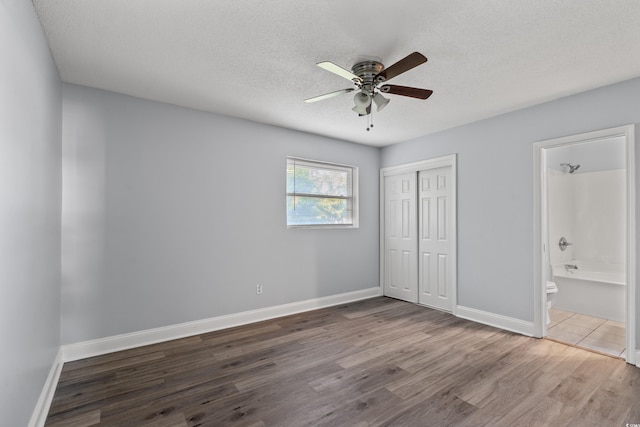 unfurnished bedroom featuring ensuite bathroom, hardwood / wood-style floors, ceiling fan, a textured ceiling, and a closet