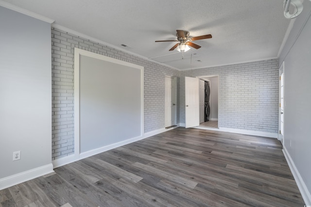 empty room featuring dark hardwood / wood-style flooring, stacked washer and dryer, crown molding, and brick wall