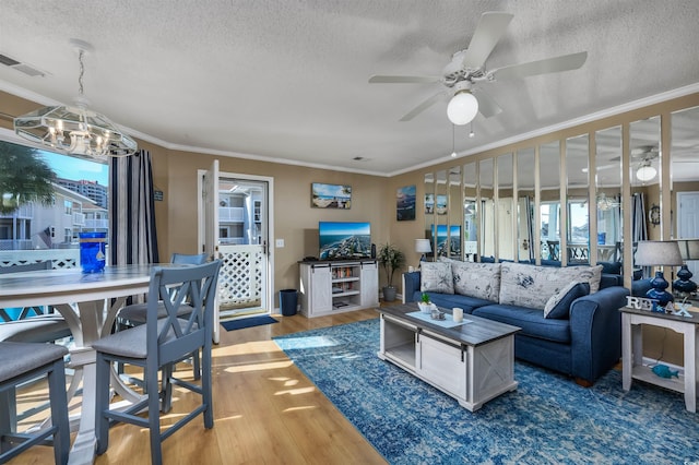 living room featuring hardwood / wood-style floors, ceiling fan with notable chandelier, ornamental molding, and a textured ceiling