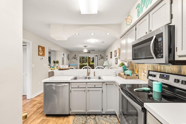 kitchen with kitchen peninsula, stainless steel appliances, ceiling fan, sink, and light hardwood / wood-style flooring