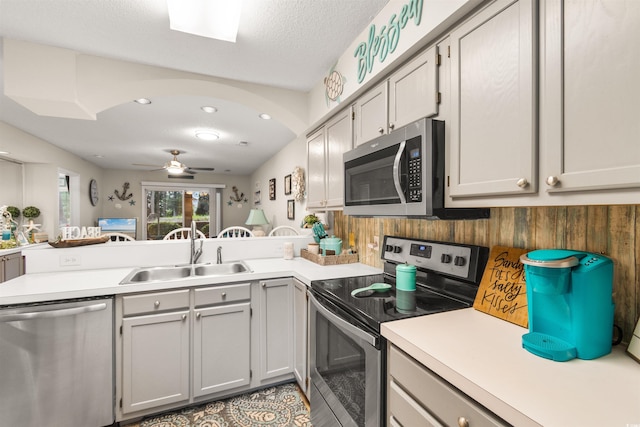 kitchen with ceiling fan, sink, kitchen peninsula, a textured ceiling, and appliances with stainless steel finishes