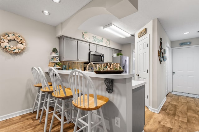 kitchen featuring kitchen peninsula, appliances with stainless steel finishes, a kitchen breakfast bar, tasteful backsplash, and gray cabinetry