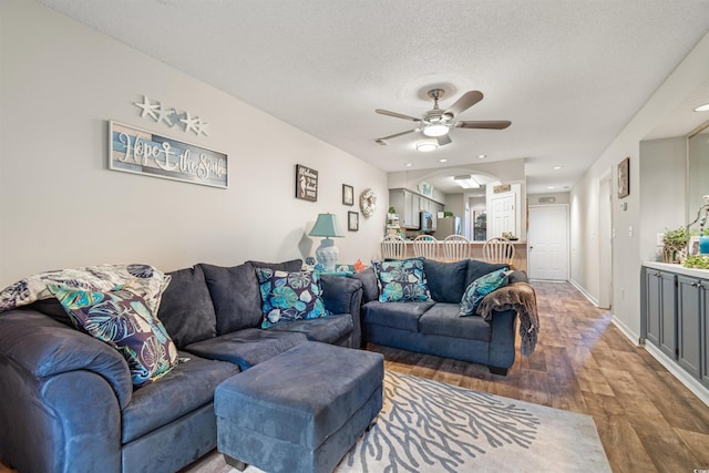 living room with a textured ceiling, ceiling fan, and dark wood-type flooring