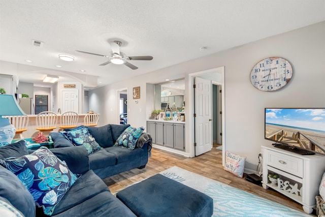 living room with ceiling fan, light hardwood / wood-style flooring, and a textured ceiling