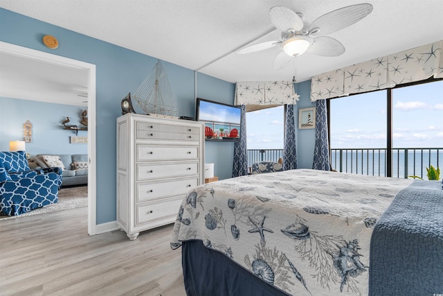 bedroom featuring access to exterior, a textured ceiling, ceiling fan, a water view, and light hardwood / wood-style floors