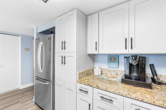 kitchen with white cabinets, light hardwood / wood-style floors, stainless steel refrigerator, and light stone counters