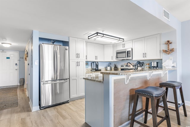 kitchen with kitchen peninsula, stainless steel appliances, white cabinetry, and stone countertops