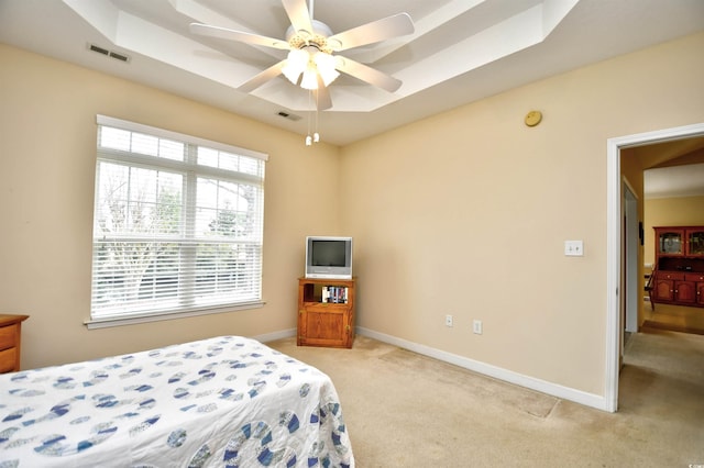 bedroom featuring ceiling fan, light colored carpet, and a tray ceiling