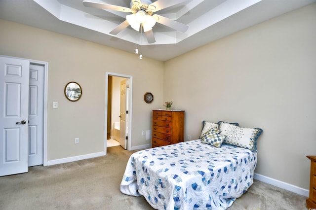 carpeted bedroom with a raised ceiling, connected bathroom, and ceiling fan