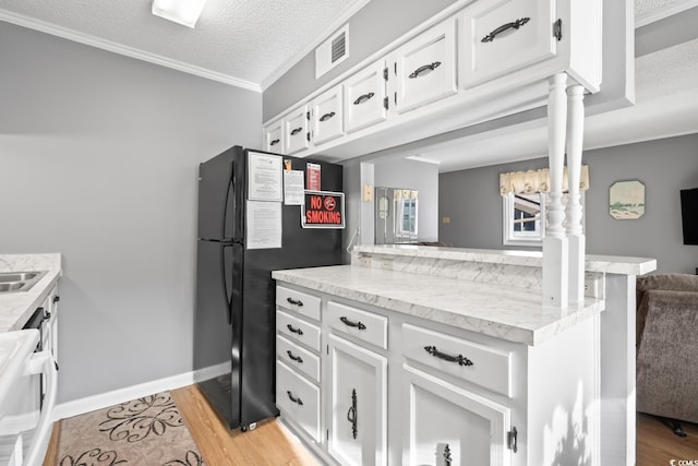 kitchen with black refrigerator, ornate columns, a textured ceiling, white cabinets, and light hardwood / wood-style floors