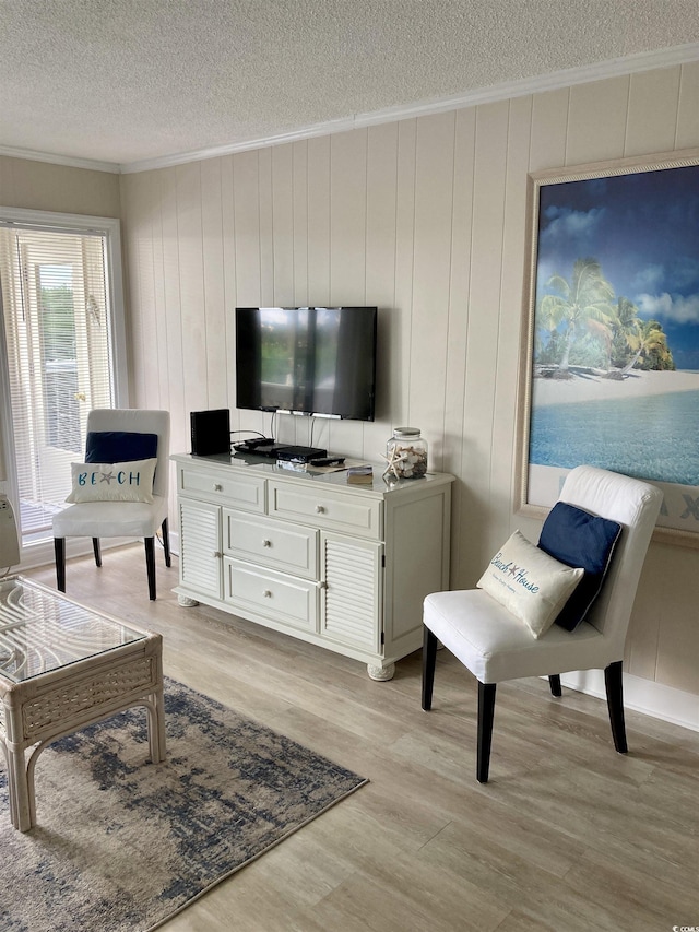 living room featuring light wood-type flooring, ornamental molding, a textured ceiling, and wooden walls