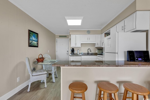 kitchen featuring sink, white refrigerator, kitchen peninsula, a breakfast bar, and white cabinets