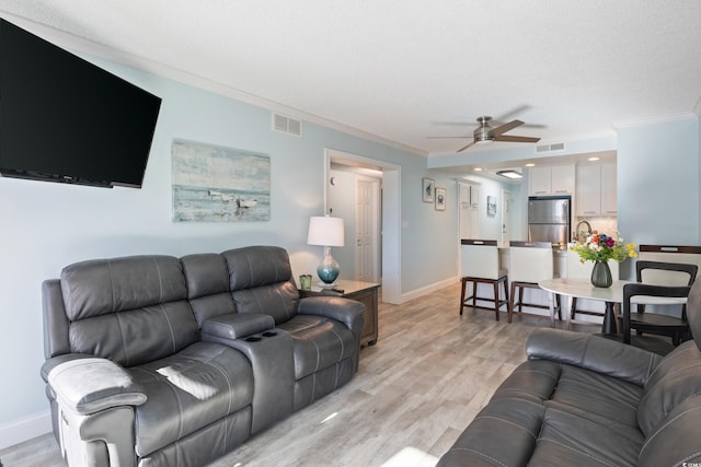 living room with ceiling fan, sink, crown molding, a textured ceiling, and light wood-type flooring