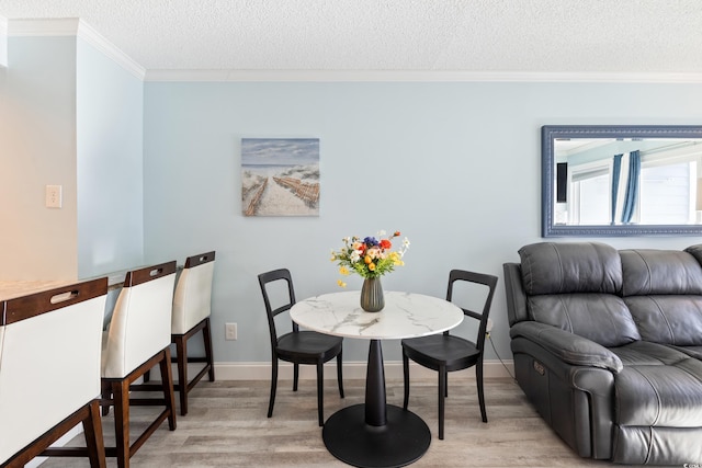 dining room with light wood-type flooring, a textured ceiling, and ornamental molding