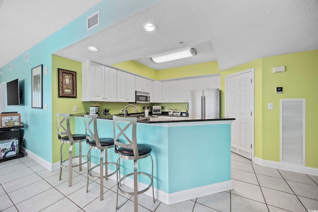 kitchen featuring white cabinets, a kitchen breakfast bar, light tile patterned flooring, kitchen peninsula, and stainless steel appliances