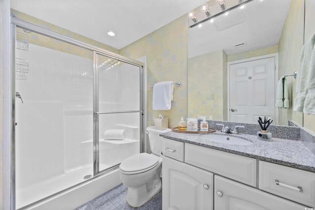 bathroom with vanity, toilet, a shower with door, and a textured ceiling