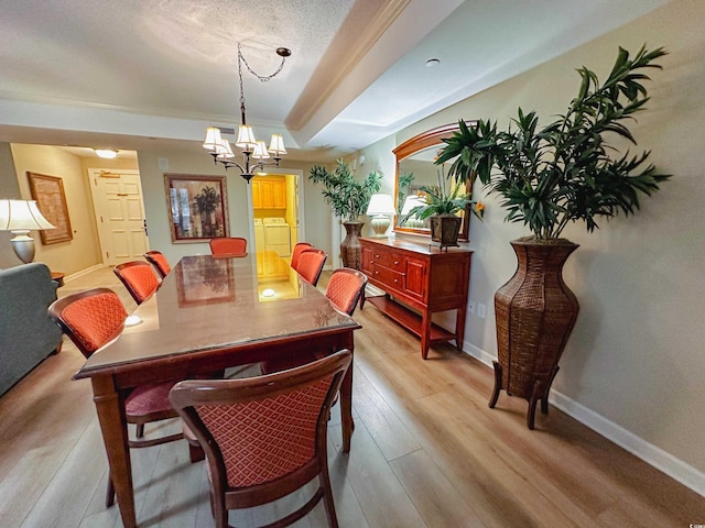 dining space featuring a textured ceiling, a raised ceiling, washer and clothes dryer, an inviting chandelier, and light hardwood / wood-style floors