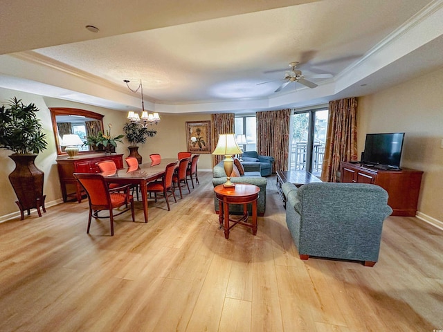 living room with ceiling fan with notable chandelier, a raised ceiling, plenty of natural light, and light wood-type flooring